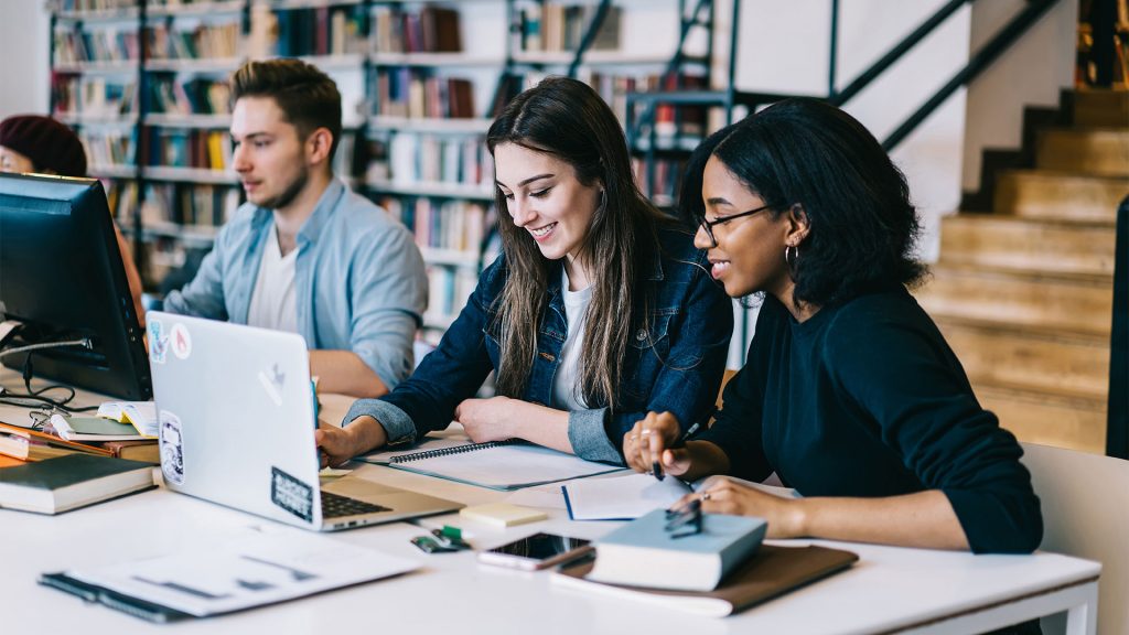 Two young women in a library looking at laptop
