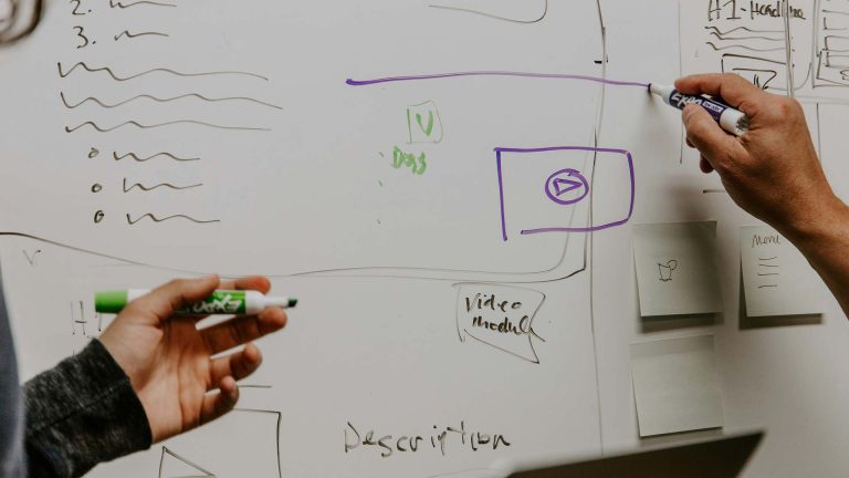 Two colleagues draw on a whiteboard as part of a meeting