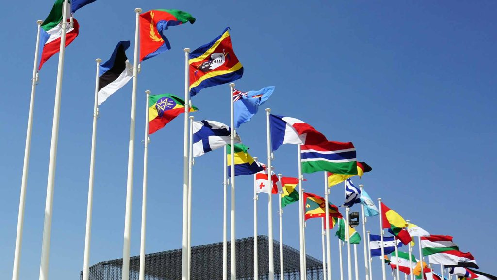 Flags of multiple countries wave in the wind atop flagpoles