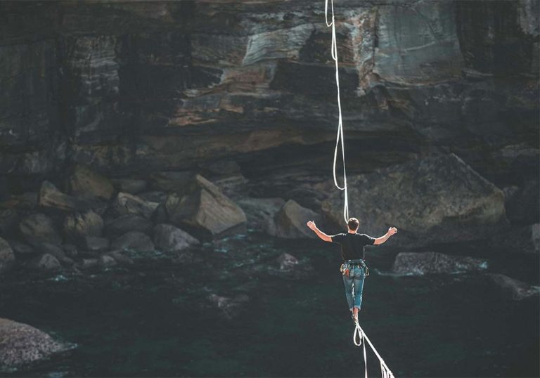 Man walking across rope between cliffs